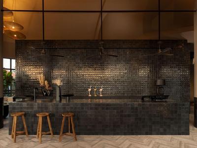 Bar scuro e moderno con sgabelli in legno e muro di mattoni neri.