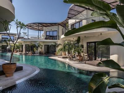 Moderner Hotelpool mit geschwungenem Design und tropischen Pflanzen in einem Urlaubsort.
