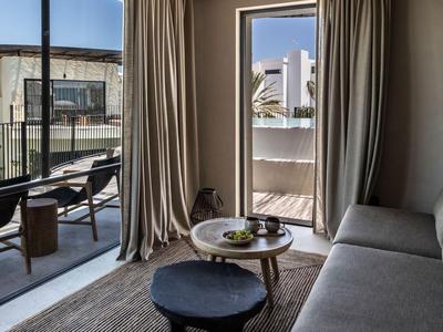 Modern eingerichtetes Hotelzimmer mit Balkon, Sofa, Tisch und Stuhl, in warmen Farbtönen.