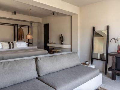 Modern eingerichtetes Hotelzimmer mit grauem Sofa, großem Bett und rustikalem Holztisch.