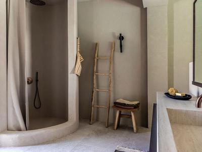 Helles Badezimmer mit abgerundeter Dusche, Holzleiter, Hocker und Waschbecken.