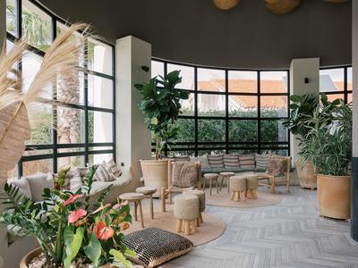 Heller Hotel-Loungebereich mit großen Fenstern, Pflanzen und gemütlichen Sitzgelegenheiten.
