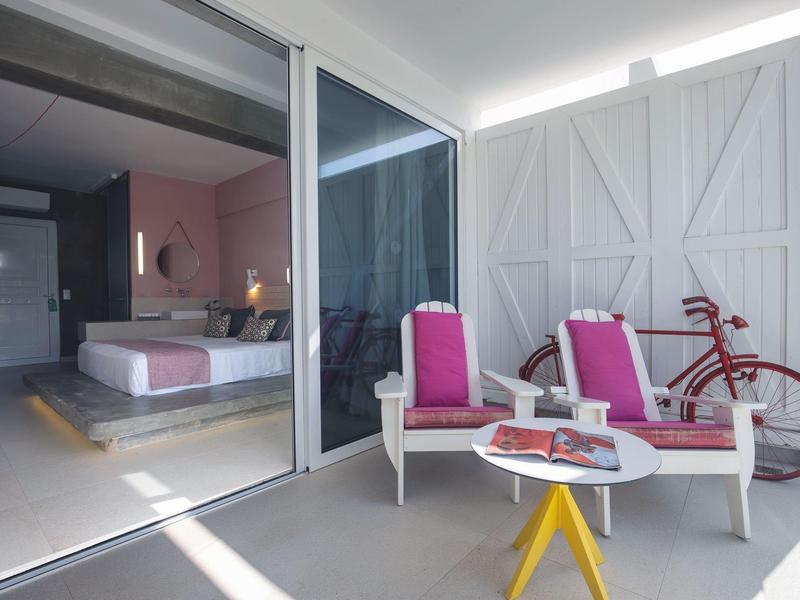 Balcone moderno dell'hotel con sedie rosa, tavolino e vista sulla camera da letto.