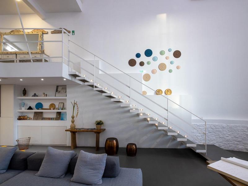 Soggiorno moderno con divano, scala bianca e decorazioni murali circolari colorate.