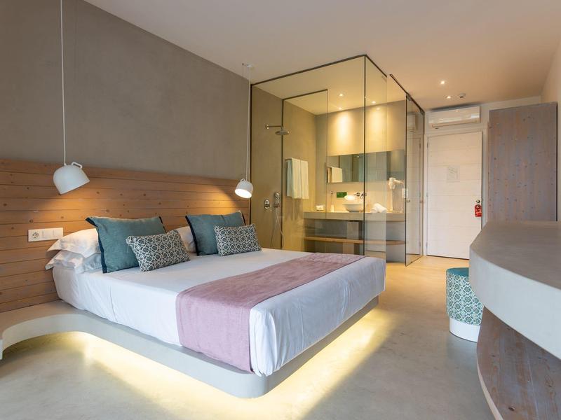 Camera d'hotel moderna con letto matrimoniale, bagno in vetro e colori neutri.