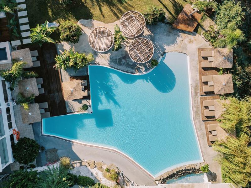 Vista aerea di una piscina dell'hotel con ombrelloni e aree relax immerse nel verde.