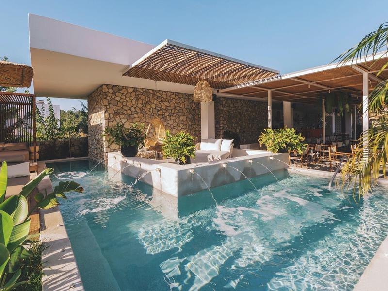 Piscina esterna moderna con area lounge e tettoia accanto a una villa in pietra.