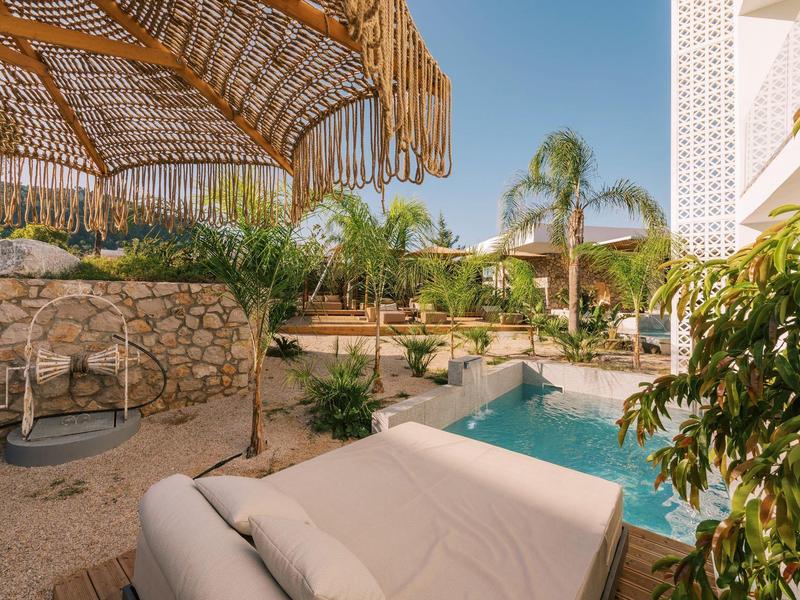 Area piscina di lusso con lettini, padiglione ombreggiato e vegetazione verde sotto un cielo limpido.