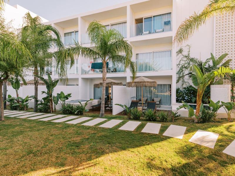 Edificio dell'hotel moderno con balcone, palme e giardino curato sotto la luce del sole.