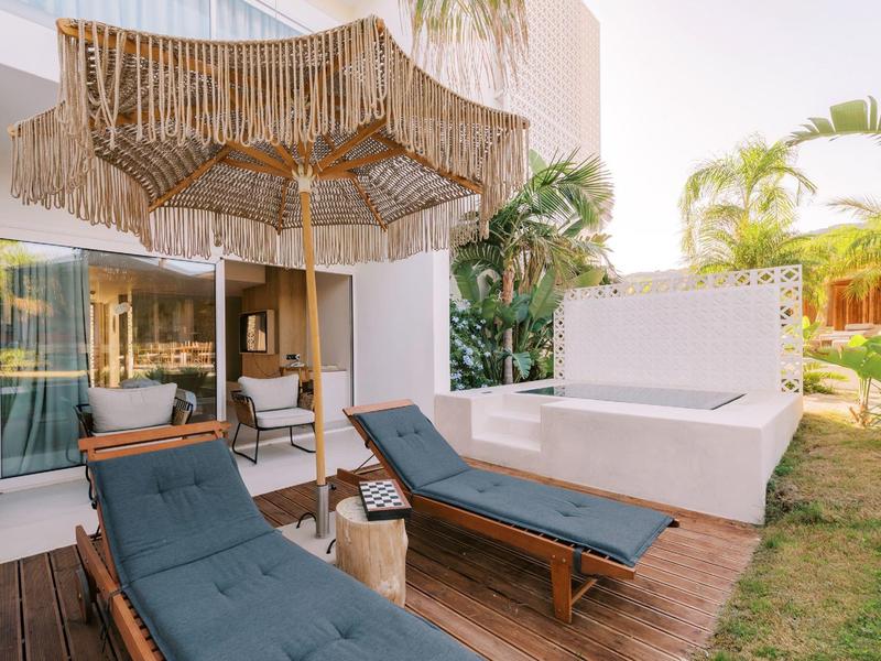 Due lettini blu accanto a una vasca da bagno esterna sotto un ombrellone.