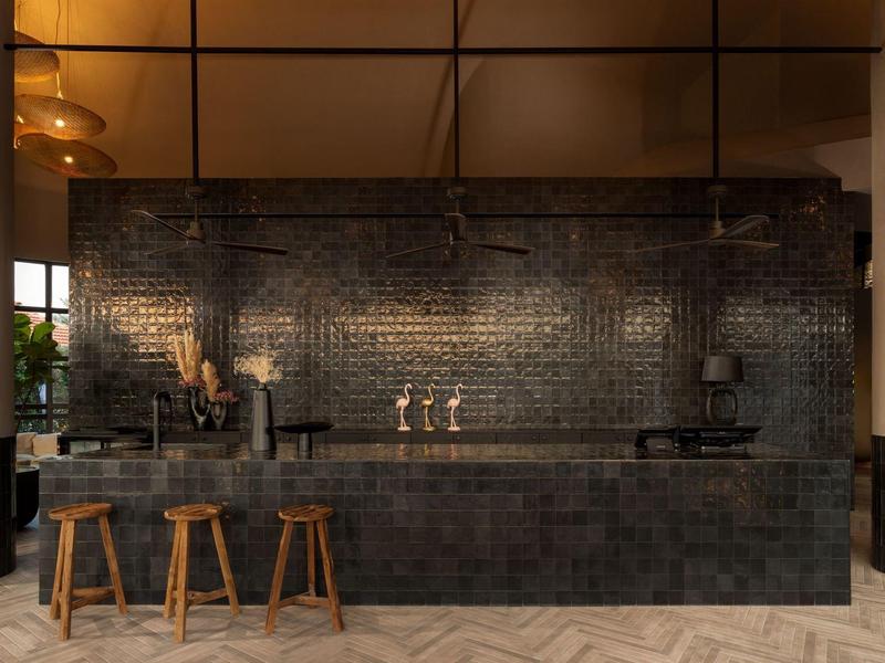 Bar scuro e moderno con sgabelli in legno e muro di mattoni neri.