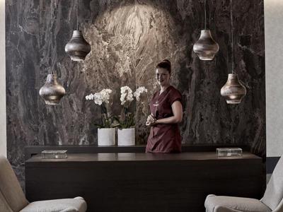 Receptionist in piedi dietro una scrivania scura con orchidee bianche e lampade sospese.