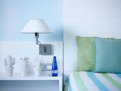 Camera luminosa con letto verde-blu, cuscini e tre piante di cactus bianche su una mensola.