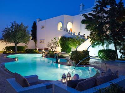 Scatto serale di una piscina illuminata davanti a un edificio bianco in un giardino mediterraneo