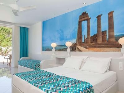 Camera d'hotel luminosa con letto matrimoniale, accenti blu e murale di colonne antiche.