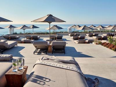 Słoneczny taras z leżakami, parasolami i widokiem na morze.