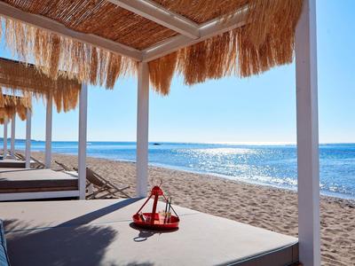 Lettini soleggiati sotto tetti di paglia con vista sul mare blu calmo.