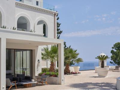Terrazza dell'hotel con palme, mobili e vista sul mare sotto un cielo azzurro.
