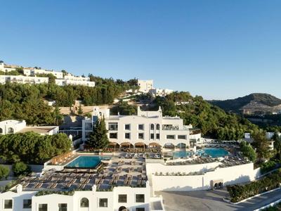 Kompleks hotelowy na wzgórzu z basenami, białymi budynkami i zielenią pod czystym niebieskim niebem.