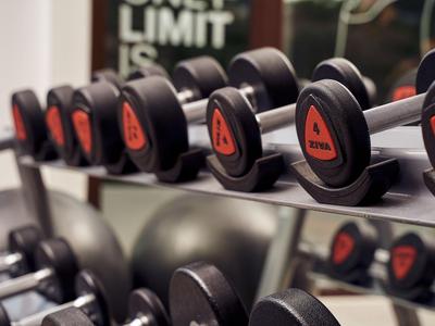 Rząd czarno-czerwonych hantli na siłowni z lustrem w tle.