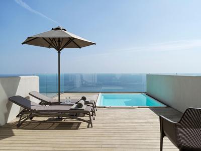 Terrazza sul tetto con lettini, ombrellone e piscina con vista mare sotto un cielo limpido.