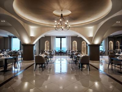 Ristorante elegante dell'hotel con archi rotondi, lampadario e vista mare attraverso grandi finestre.
