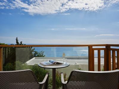 Balkon s dvěma židlemi a stolem s výhledem na moře pod jasnou oblohou.