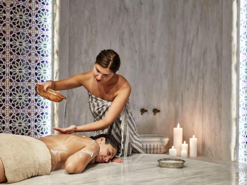 Donna che riceve un massaggio benessere in una spa lussuosa con candele in stile orientale.