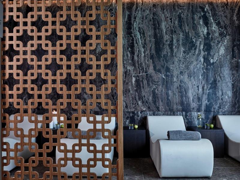 Area benessere moderna con separé decorativo in legno e poltrone bianche davanti a parete in marmo.