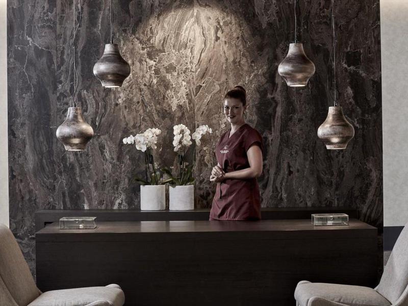 Receptionist in piedi dietro una scrivania scura con orchidee bianche e lampade sospese.