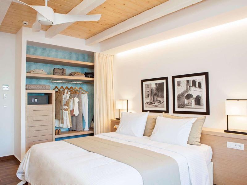 Camera d'hotel moderna con letto matrimoniale, armadio aperto e illuminazione elegante.