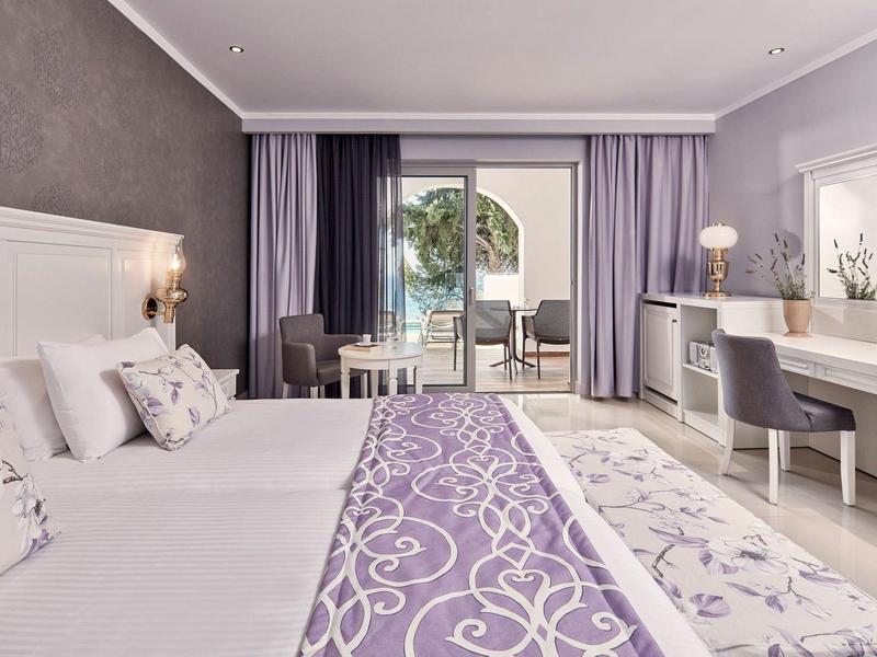 Camera d'hotel moderna con letto matrimoniale, scrivania e balcone con vista sul giardino.