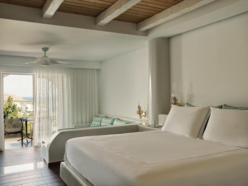 Camera d'hotel luminosa con due letti matrimoniali, soffitto con travi in legno e balcone con vista mare.