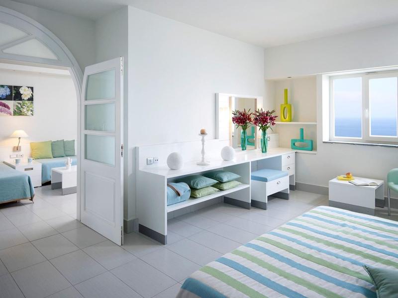 Camera d'hotel luminosa con vista mare, letto matrimoniale, zona soggiorno e salotto adiacente.