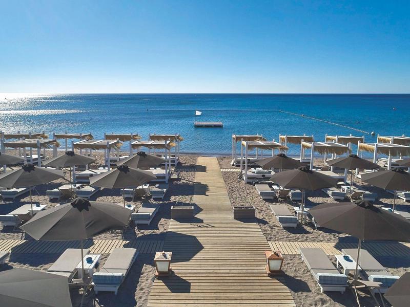 Spiaggia vuota con lettini e ombrelloni di fronte a un mare calmo e blu sotto un cielo sereno.