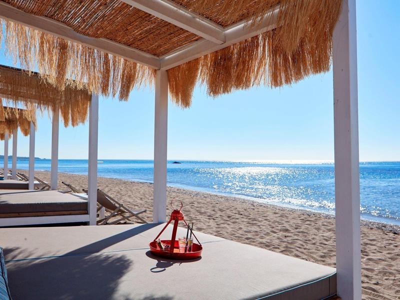 Lettini soleggiati sotto tetti di paglia con vista sul mare blu calmo.