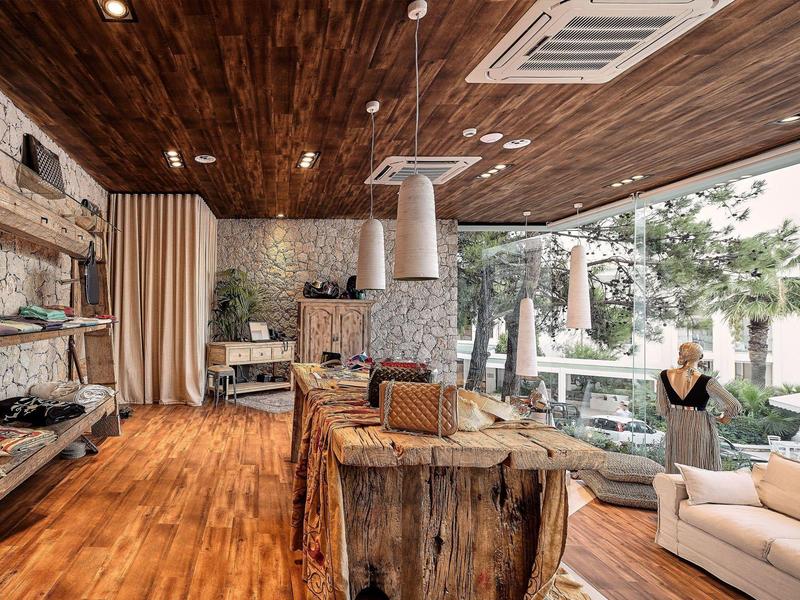 Accogliente area lounge con soffitto in legno, pareti in pietra e grandi finestre con vista sulle palme.