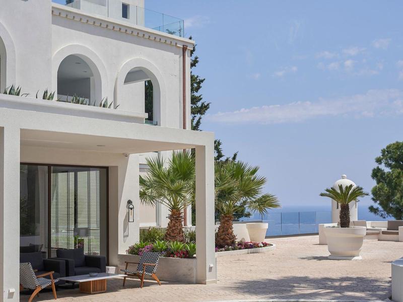 Terrazza dell'hotel con palme, mobili e vista sul mare sotto un cielo azzurro.