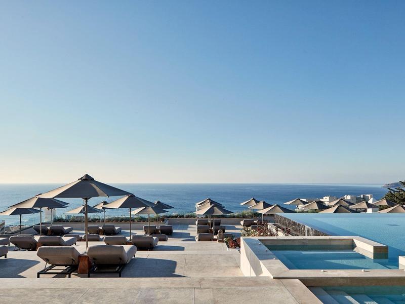 Area piscina di lusso con lettini e ombrelloni sul mare sotto un cielo limpido.