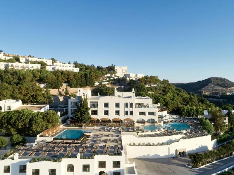 Hotel bianco di lusso con piscine su una collina e vista sulle montagne con cielo limpido.