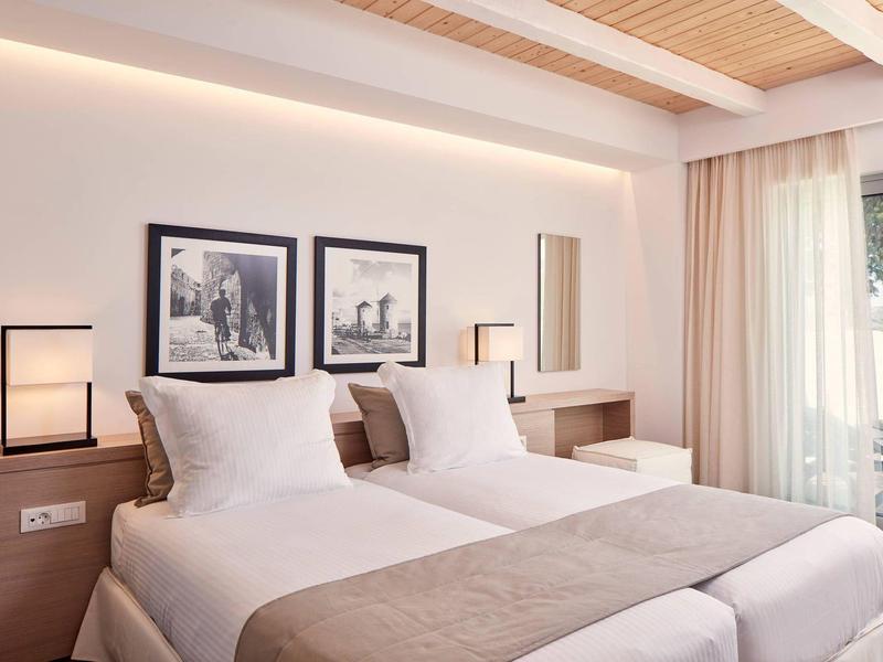 Camera d'hotel luminosa con due letti singoli, lampade moderne e vista sul balcone.