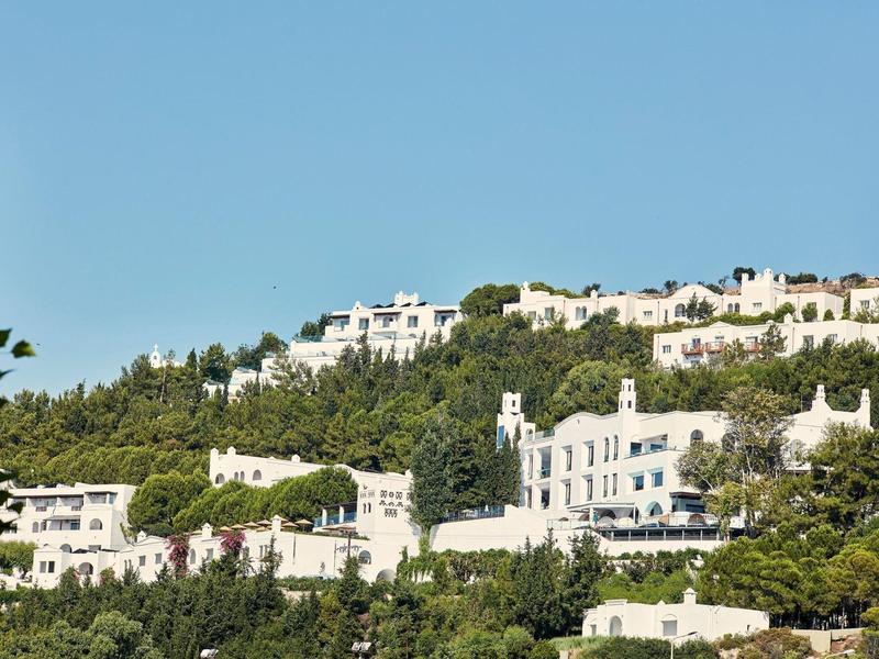 Vista di edifici bianchi su colline verdi sotto un cielo blu chiaro.