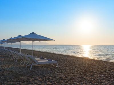 Strand mit Liegestühlen und Sonnenschirmen bei Sonnenuntergang am Meer.
