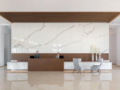 Area reception moderna con parete in marmo, scrivania in legno e due poltrone grigie.