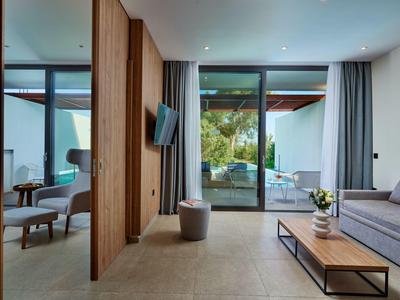 Camera d'hotel moderna con divano, poltrona e vista sulla terrazza con piscina.