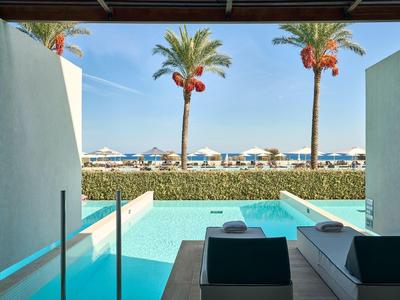 Vista da un balcone moderno con piscina su palme e spiaggia sabbiosa con ombrelloni.