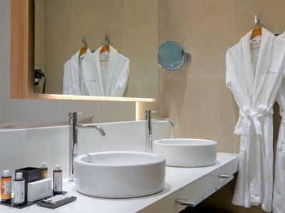 Bagno moderno con due lavabi, specchi e accappatoi bianchi appesi al muro.