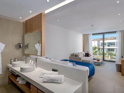 Camera d'hotel moderna con bagno aperto, letto matrimoniale e balcone con vista sul giardino.