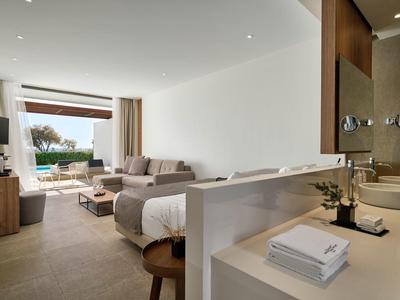 Camera d'hotel luminosa con letto, divano, TV e vista sulla piscina e terrazza.