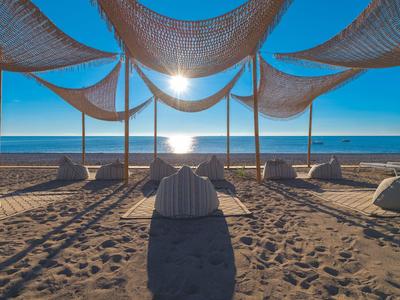 Sonnige Strandansicht mit Sitzsäcken unter Sonnensegeln und Meer im Hintergrund.